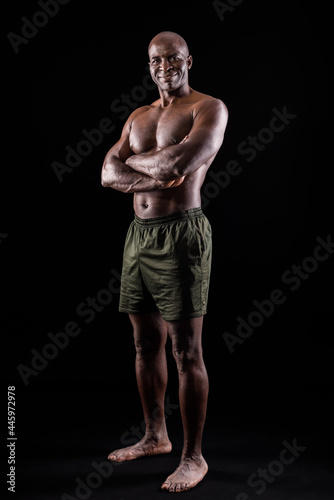 Adult African American in shorts standing with arms crossed, black background