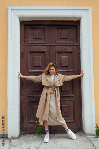 Young millennial woman with wild hair dressed in an autumn coat posing near the door of an old building. © Smile