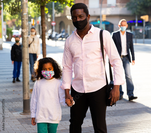 African american man in protective mask walking with his cute preteen daughter along city street on warm fall day. New life reality during coronavirus pandemic