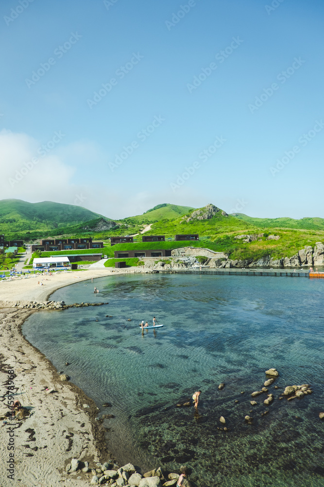 summer sea panorama. shallow, clear, transparent sea with reefs, rocks and and holiday houses on the green summer hills. Japan sea.