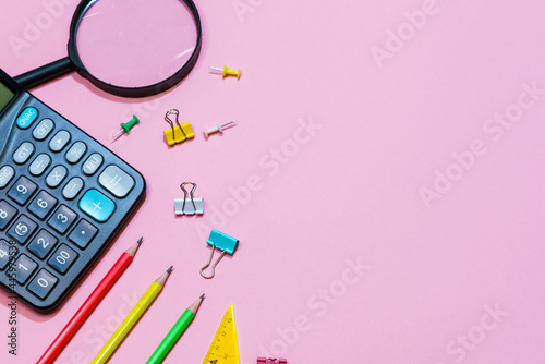 Various office supplies on a pink background. Back to school concept. View from above. Calculator and pencils