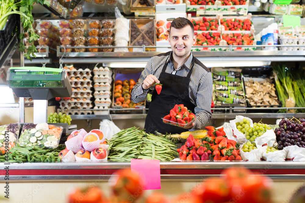 professional male seller showing assortment of fruits and vegetables in the grocery shop