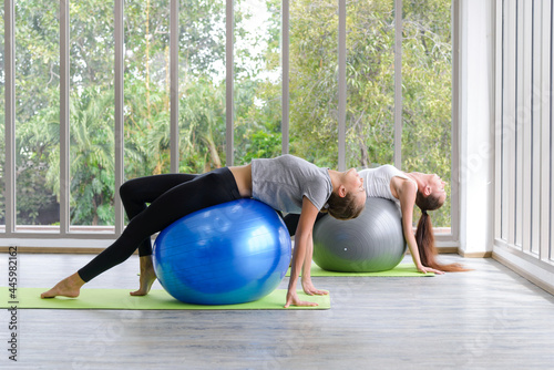 Two caucasian women exercising with exercise ball. Fitness girls flexing abdominal muscles with fit ball in gym room