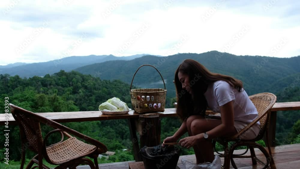 An asian woman preparing and lighting fire in a stove before cooking Moo Kata, Thai barbecue grill pork on balcony with beautiful nature view An asian woman preparing and lighting fire in a stove before cooking Moo Kata, Thai barbecue grill pork on balcony with beautiful nature view