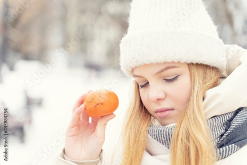 young beautiful woman is sad in winter. holding an orange with a painted sad face in his hand