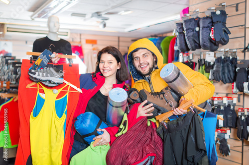Young loving couple demonstrating the tourist equipment in sports clothes store. Focus on both persons