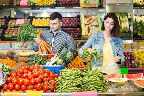 Young joyous couple choosing fresh vegetables in grocery shop