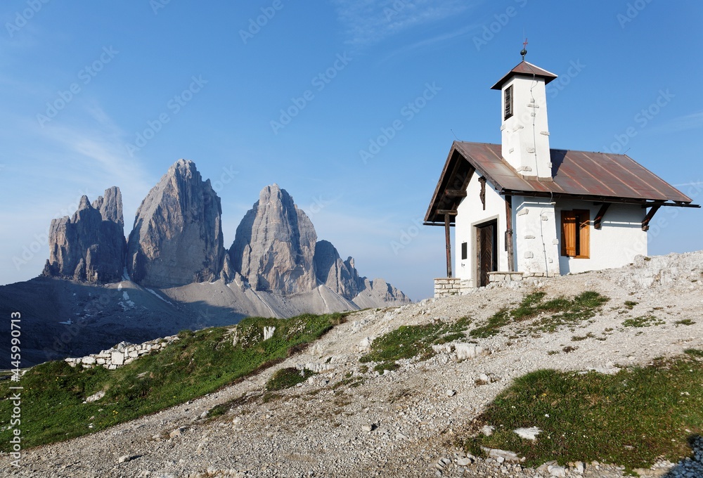 Summer scenery of a lovely chapel under blue clear sky, with the magnificent vertical peaks of Tre Cime di Lavaredo ( Drei Zinnen ) in the background, in Sexten Dolomites, South Tyrol, Italy, Europe