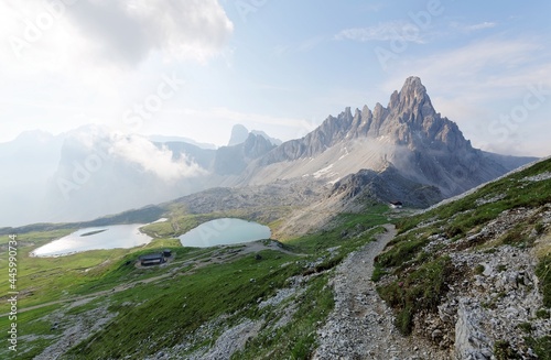 Majestic scenery of Alpine Lakes (Laghi del Piani) at foothills of Mountain Paternkofel (Monte Paterno) and a hiking trail by the mountainside on a foggy summer morning in Dolomiti, South Tyrol, Italy