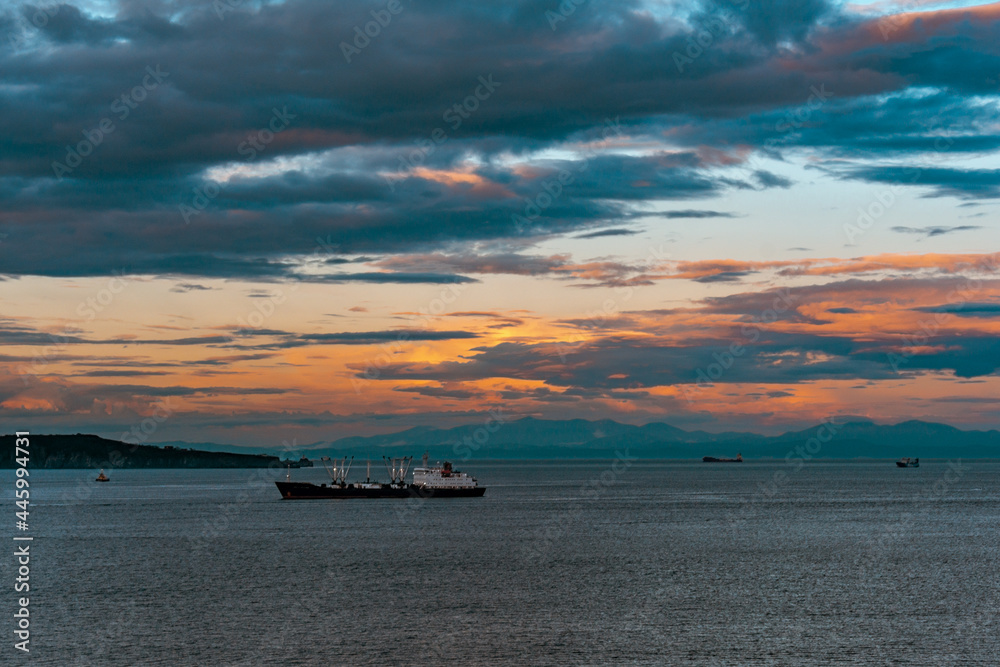 Ship at sea and sunset in the sky with clouds during dusk