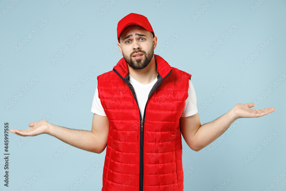 Professional sad tired worry delivery guy employee man in red cap white T-shirt vest uniform workwear work as dealer courier isolated on pastel blue color background studio portrait. Service concept.