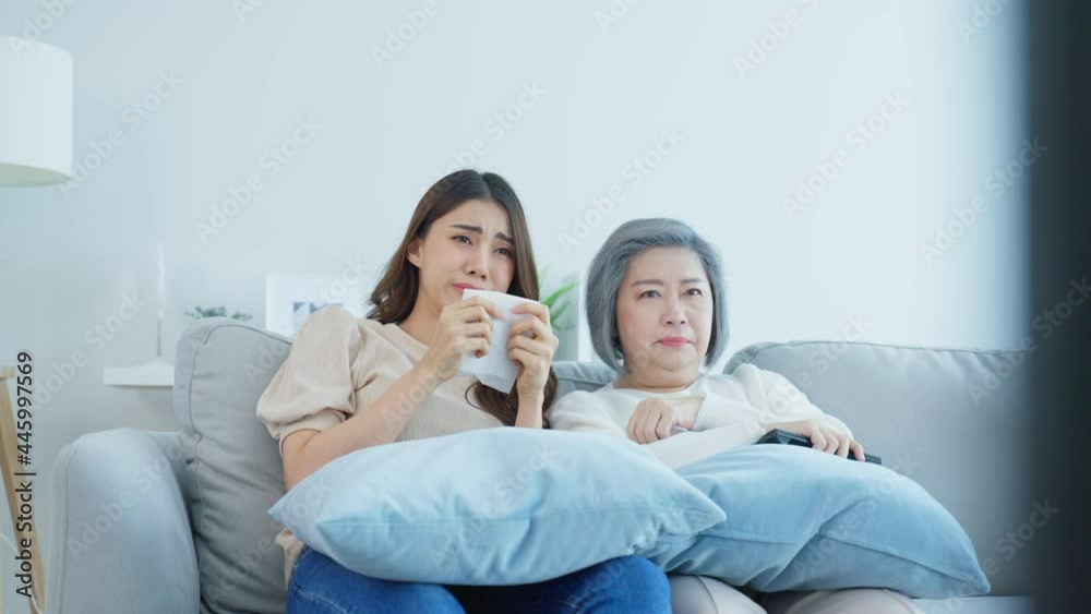 Asian senior mature woman and daughter sitting on sofa watch sad movie Asian senior mature woman and daughter sitting on sofa watch sad movie