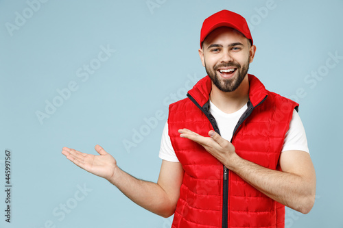 Delivery guy employee man in red cap white T-shirt uniform workwear work as dealer courier recommend suggest select promo area advert isolated on pastel blue color background studio. Service concept.