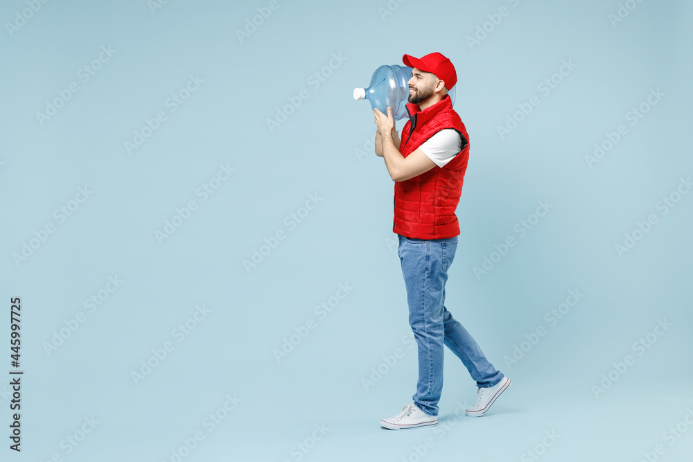 Full size body length side view delivery guy man in red cap white T-shirt vest uniform workwear work dealer courier hold water bottle isolated on pastel blue color background studio Service concept Full size body length side view delivery guy man in red cap white T-shirt vest uniform workwear work dealer courier hold water bottle isolated on pastel blue color background studio Service concept