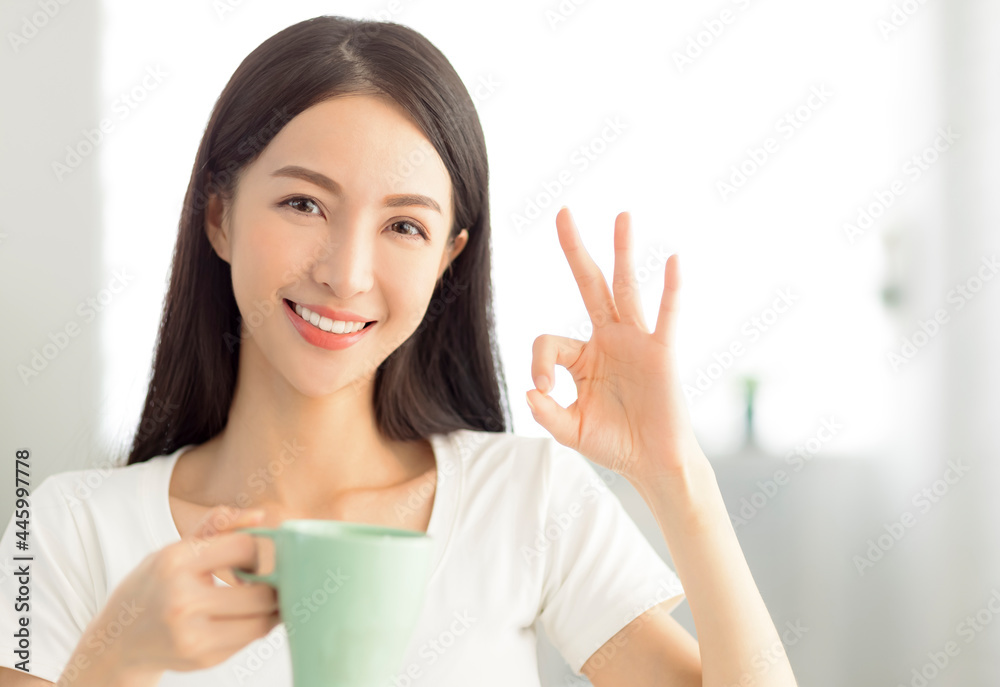 Smiling young woman holding coffee cup and showing ok gesture Smiling young woman holding coffee cup and showing ok gesture