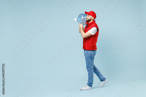 Full size body length side view delivery guy man in red cap white T-shirt vest uniform workwear work dealer courier hold water bottle isolated on pastel blue color background studio Service concept