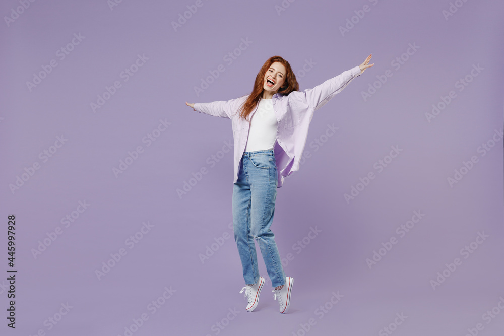 Full size body length young redhead curly woman 20 wear white T-shirt violet jacket stand on toes dance lean back have fun spread hands isolated on pastel purple color wall background studio portrait