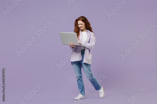 Full size body length cute young redhead curly green-eyed woman 20 wear white T-shirt violet jacket hold use work on laptop pc computer isolated on pastel purple color wall background studio portrait