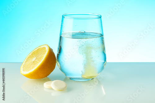 effervescent vitamin C tablet dissolves in water. a glass of water, effervescent tablet and citrus fruit on blue background. vitamin C concept