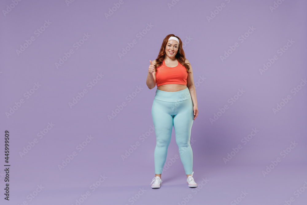 Full length young fun chubby overweight plus size big fat fit woman wear red top warm up training show thumb up gesture isolated on purple background studio home gym. Workout sport motivation concept. Full length young fun chubby overweight plus size big fat fit woman wear red top warm up training show thumb up gesture isolated on purple background studio home gym. Workout sport motivation concept.