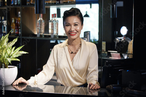 Portrait of smiling elegant restaurant owner in silk blouse standing behid bar and looking at camera photo