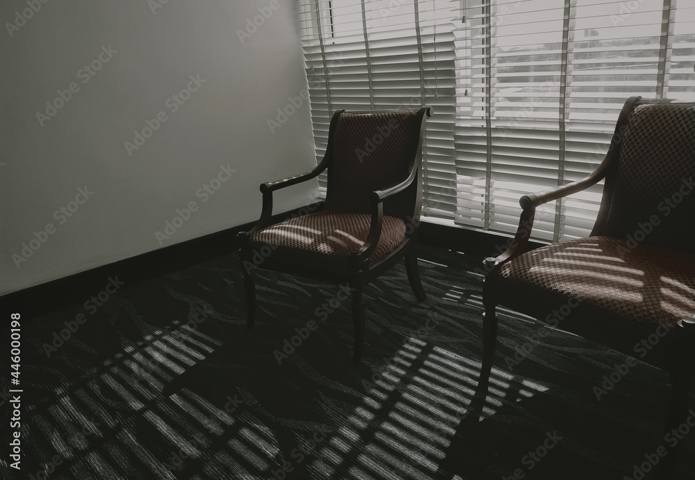 Empty chairs with light and shadow in the room. Furniture for home decoration in vintage style. Empty couple of chair in living room stand on carpet floor near Venetian plastic blinds. Wooden chair. Empty chairs with light and shadow in the room. Furniture for home decoration in vintage style. Empty couple of chair in living room stand on carpet floor near Venetian plastic blinds. Wooden chair.