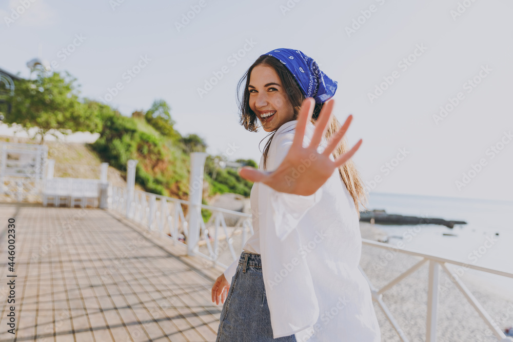 Young side view excited smiling happy traveler tourist woman 20s in blue bandana shirt summer casual clothes rest covering with hands outdoors at sea beach People vacation lifestyle journey concept.