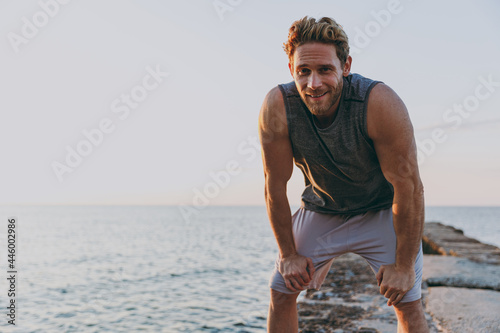 Foto Tired satisfied young strong sporty athletic toned fit sportsman man 20s in sports clothes warm up train look far away at sunrise sun dawn over sea beach outdoor on pier seaside in summer day morning