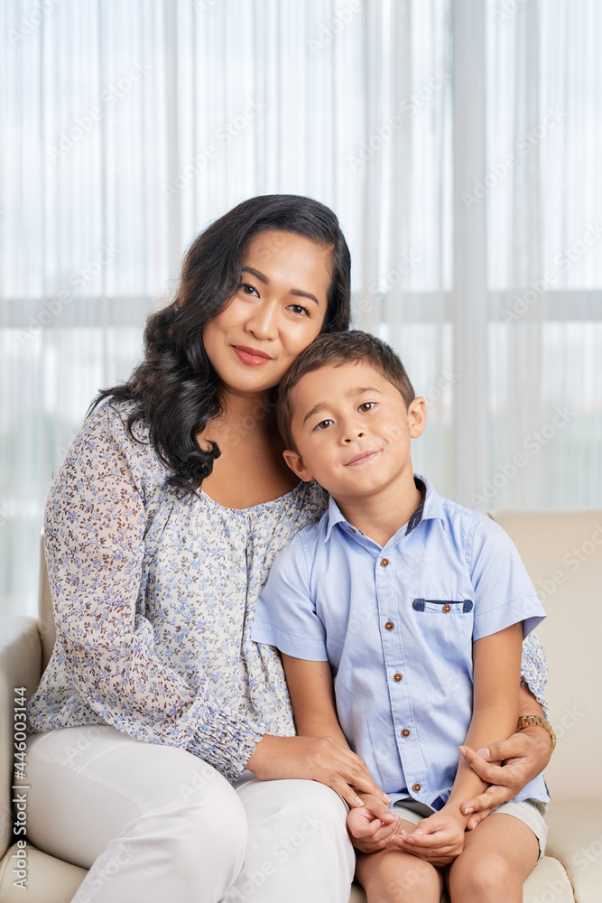 Portrait of Asian young woman sitting together with her little son in the room and looking at camera Portrait of Asian young woman sitting together with her little son in the room and looking at camera
