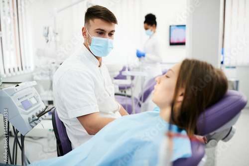 Young dentist communicating with patient before dental exam at dentist s office.