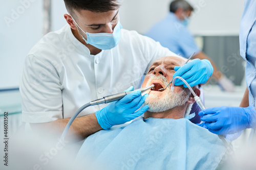 Young dentist using dental polish on senior man's teeth during exam at dentist's office.
