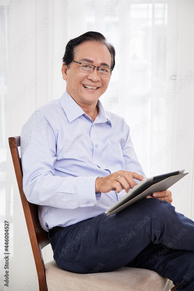 Portrait of happy smiling senior businessman sitting on chair and using application on digital tablet Portrait of happy smiling senior businessman sitting on chair and using application on digital tablet