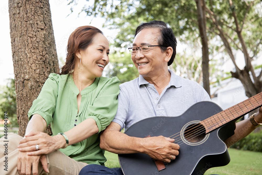 Cheerful senior couple resting in park, they are playing guitar, singing and looking at each other