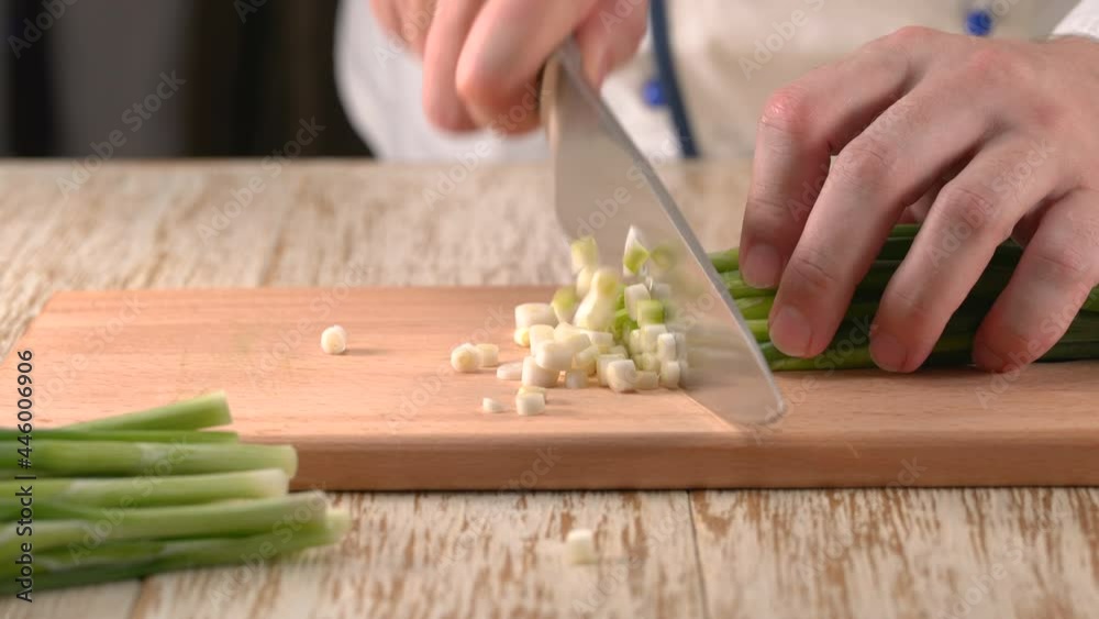 Сhief-cook chopping fresh green onion on a wooden cutting board, close up. Chef's hands with knife cutting fresh spring onion. Сhief-cook chopping fresh green onion on a wooden cutting board, close up. Chef's hands with knife cutting fresh spring onion.