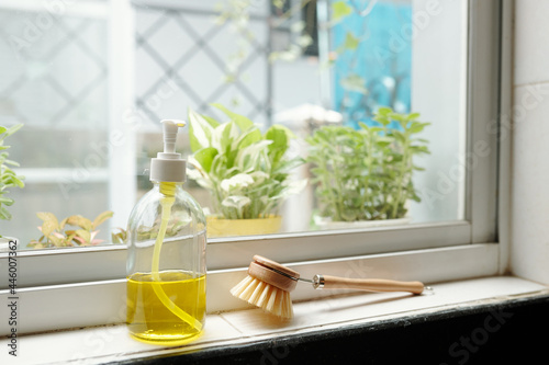 Bottle of yellow dish soap and brush on window sill in kitchen photo