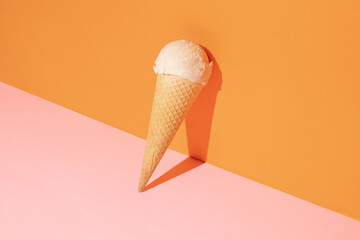 Creative compostition made with ice cream vanilla scoop and cone against pastel pink and orange background. Retro aesthetic style. Summer life style idea.