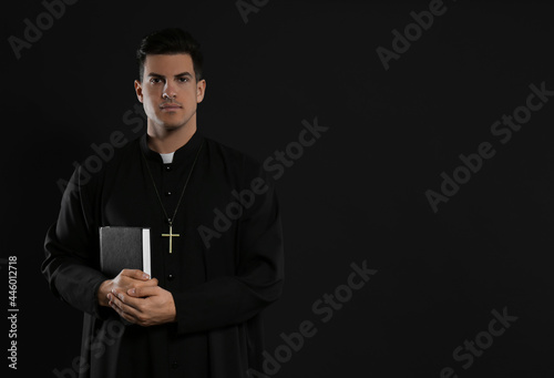 Schilderij op canvas Priest with Bible on black background. Space for text