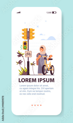 arab schoolgirl with bicycle waiting for green traffic light to cross road on crosswalk road safety concept vertical