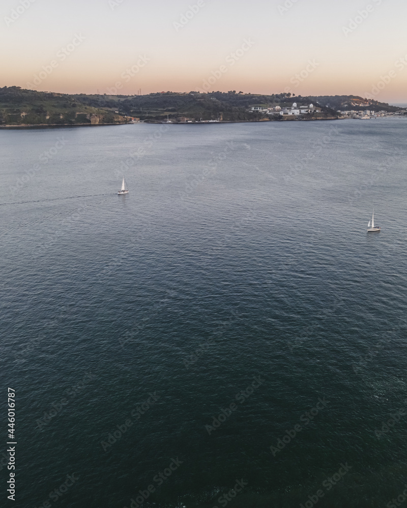Aerial view of two small sailing boat crossing the Tagus river at sunset, Lisbon, Portugal