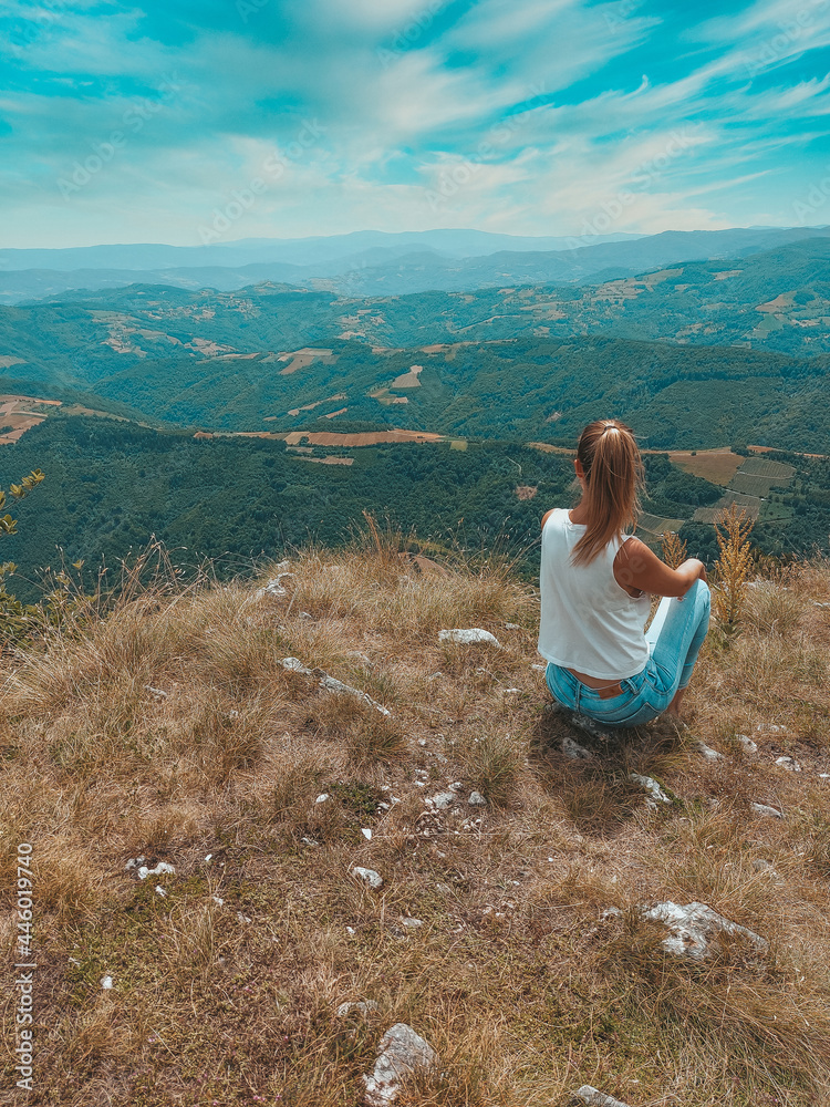 Woman contemplating a beautiful landscape. Happy Woman Enjoying Nature on meadow on top of mountain. Outdoor. Freedom concept. Rear view of a young woman sitting on a mountain top