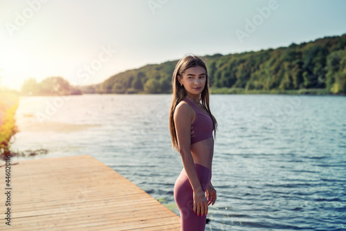 Young slim woman wearing sport clothing rest after morning exercise near lake