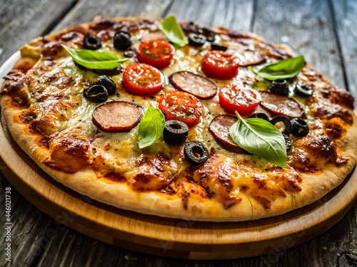 Pizza with white mushrooms, sausage, tomatoes, black olives, parmesan and mozzarella on wooden background 