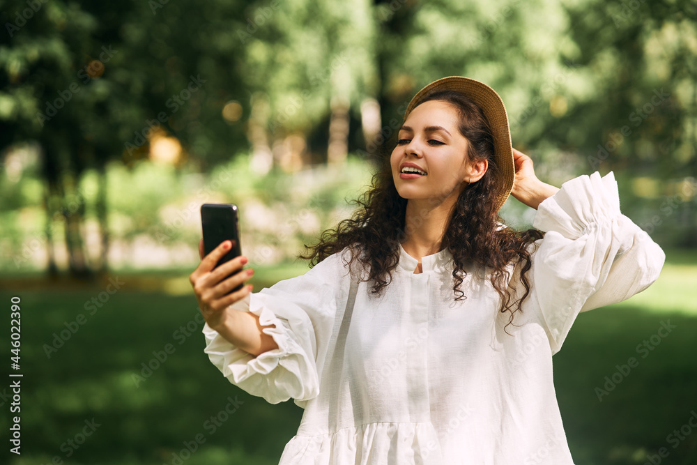 Young beautiful girl in a hat makes a selfie on her phone in the park Young beautiful girl in a hat makes a selfie on her phone in the park