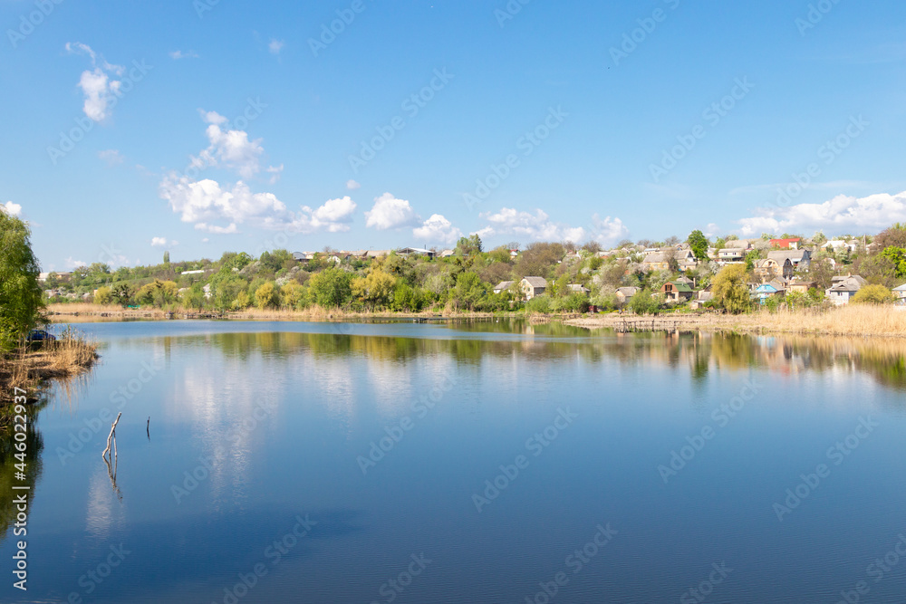 green coast of a beautiful small river with white clouds in reflection