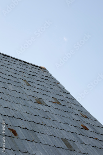A minimalist photograph of a house roof against a clear blue sky. The roof is covered with metal tiles.