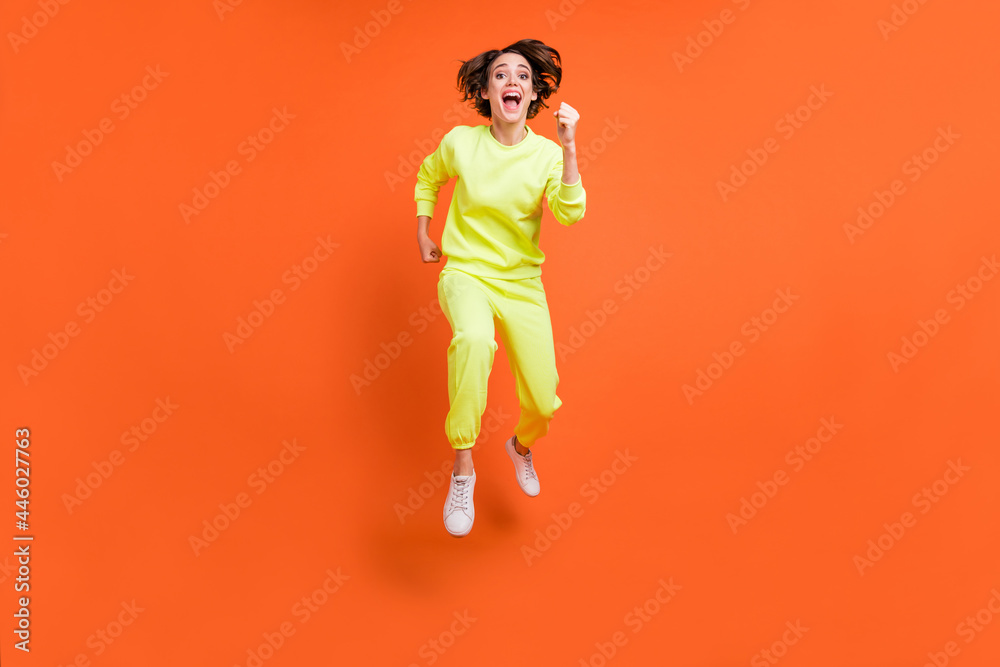 Full length body size view of attractive cheerful motivated girl jumping running marathon isolated over bright orange color background Full length body size view of attractive cheerful motivated girl jumping running marathon isolated over bright orange color background