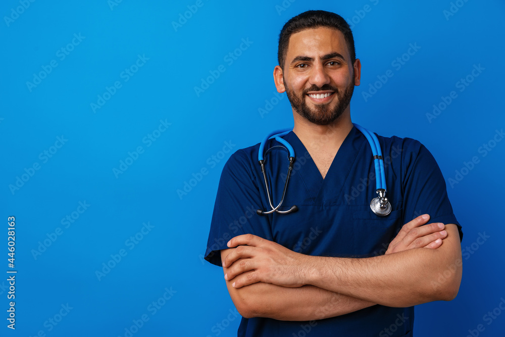 Handsome young male doctor in blue uniform with stethoscope against blue background Handsome young male doctor in blue uniform with stethoscope against blue background