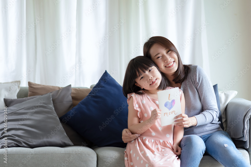 Asian mother hug her cute daughter that give handmade greeting card with i love mom word to surprising her at home