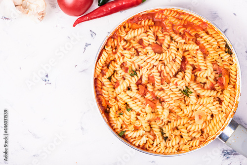 Girandole pasta with hot red tomato sauce in a frying pan and ingredients for making the sauce on the table, copy space