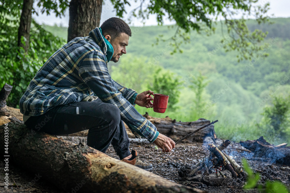 A man on a hike sits by the fire and warms himself. A man on a hike sits by the fire and warms himself.